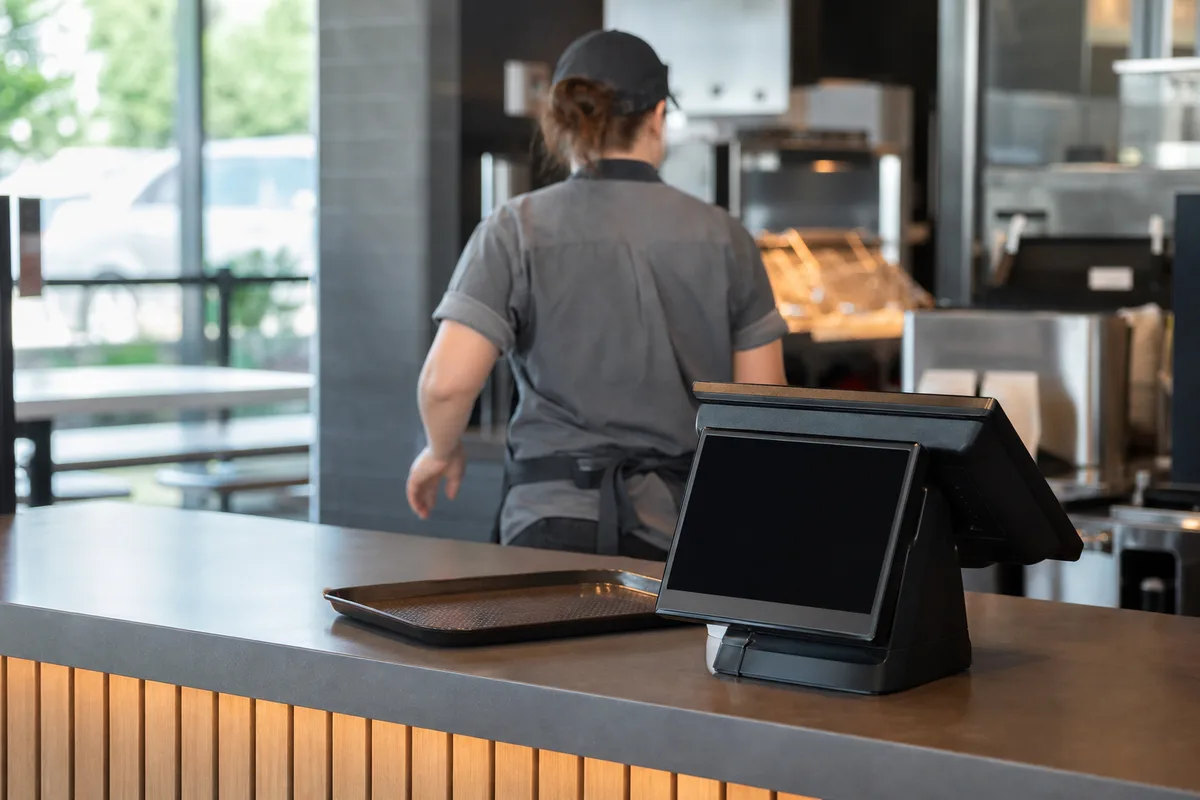 Comptoir de commande d’un fast-food avec caisse tactile et vue sur la cuisine d’assemblage